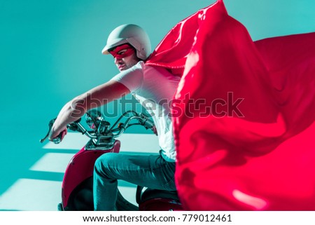 side view of man in protective helmet and superhero costume on red scooter