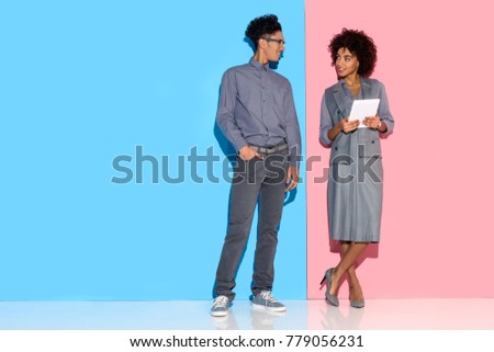 Young african amercian businessman standing by girl with tablet in hands on pink and blue background 
