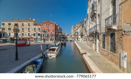 A view of Venice timelapse: canal, bridge, boats and an old tower in the background. Blue sky at summer day. People walking around
