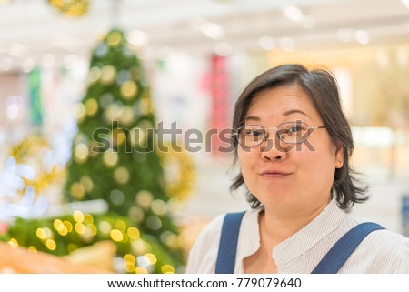 Asian woman 40s white skin plump body with backpack waiting in department store or shopping mall with pine tree in merry christmas and new year celebration