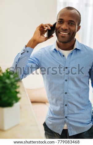 In high spirits. Good-looking alert young man talking on the phone and beaming and enjoying the conversation