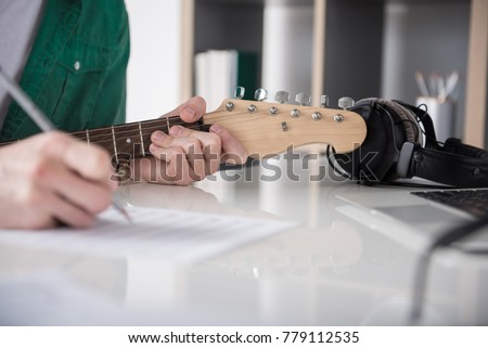 Close up of musician writing music on paper. Focus on his fingers doing accord on guitar