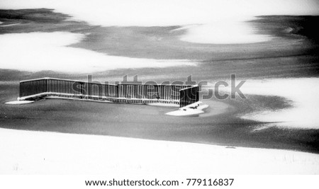 Metal fence, pier flooded with water and covered with ice. Winter nature. Snow drawing on the lake.