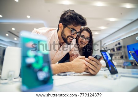 Close up focus view of a cheerful charming happy young student love couple choosing a new mobile in a tech store. Royalty-Free Stock Photo #779124379