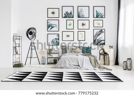 Black and white carpet in spacious monochromatic bedroom with lamp, king-size bed and chair against wall with posters