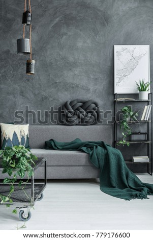 Dark green blanket on grey sofa against concrete wall in guy room interior with designer lamp and map poster on the wall Royalty-Free Stock Photo #779176600