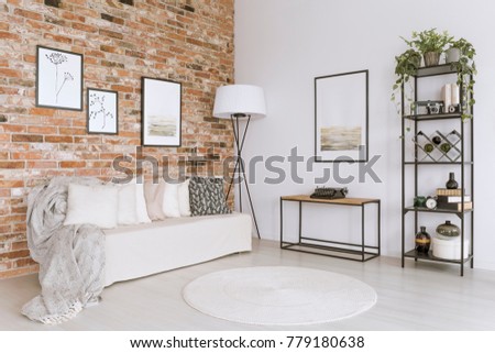 White sofa with pillows and white carpet in living room with lamp against red brick wall with gallery