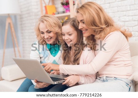 Mom, grandmother and girl are looking at something on the laptop screen. They are in a good mood. They are smiling.
