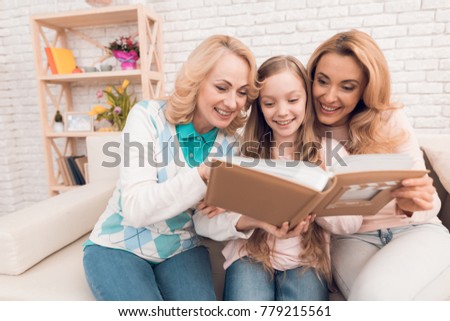 Mom, grandmother and girl are considering a family album. They are in a good mood. They are smiling.