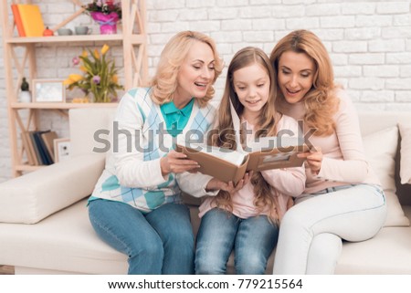 Mom, grandmother and girl are considering a family album. They are in a good mood. They are smiling.