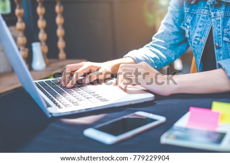 Woman hand works in a laptop computer in the office.On the table are mobile phones.Sunlight shines on the keyboard.