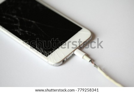 Broken old smartphone with broken display or crack screen, charge the battery with torn wire on white background