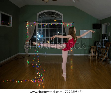 Young teenage ballerina wearing a red leotard, tights and pointe shoes in a dance studio with Christmas lights.