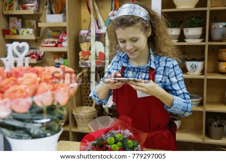 Young beautiful smiling woman florist is taking a picture of bouquet in florist shop