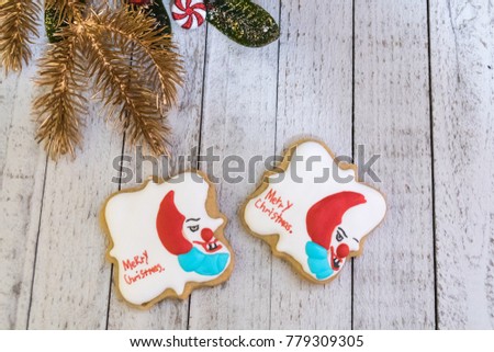 Evil creepy scary clown homemade decorated sugar cookies, with the phrase Merry Christmas written on them. Whitewashed wood background