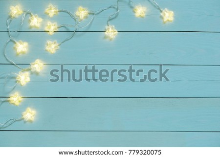 Gleam of an electric garland with star bulbs on a blue wooden background. 