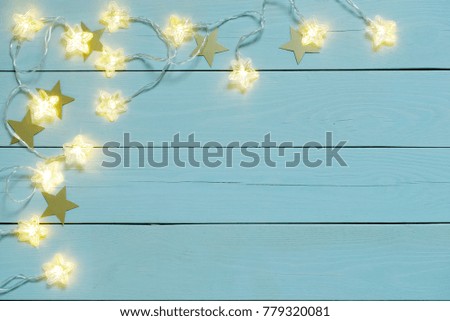 Gleam of an electric garland with star bulbs on a blue wooden background. 