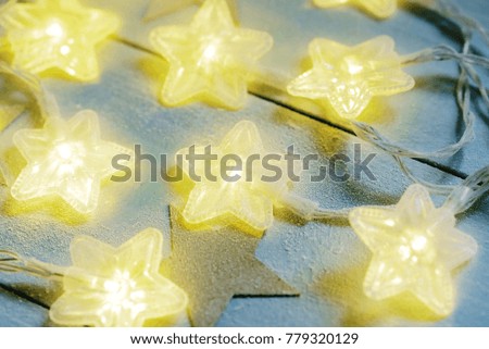Gleam of star twinkle lights covered with frost on a blue wooden background, closeup.