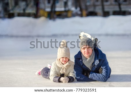 Smiling young father and her cute little daughter ice skating together