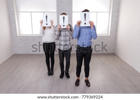 Two guys and a girl stand indoors and cover their faces of sheets with a exclamation point.