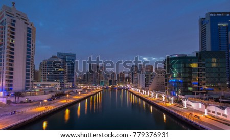 Vew of Dubai Marina embankment with Towers and yachts from bridge in Dubai night to day transition timelapse, United Arab Emirates. Dubai Marina is a district in Dubai and an artificial canal city. 