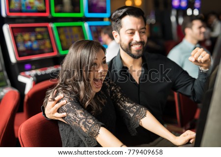 Good looking young couple celebrating and looking excited about hitting the jackpot in a slot machine at a casino Royalty-Free Stock Photo #779409658
