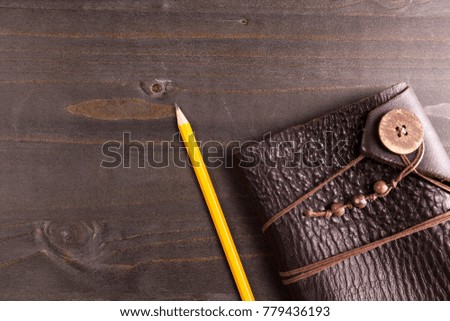 Top view of a notebook and a pencil next to it on wooden backgorund