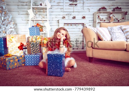 Pretty young girl dreaming of christmas as she rests her chin on top of a decorative gift in a home decorated for new year christmas party