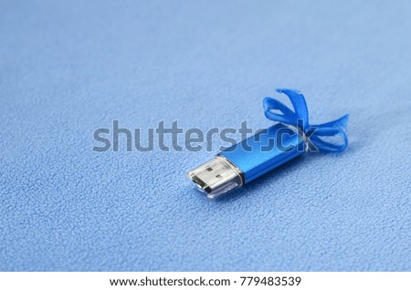 Brilliant blue usb flash memory card with a blue bow lies on a blanket of soft and furry light blue fleece fabric. Classic female gift design for a memory card