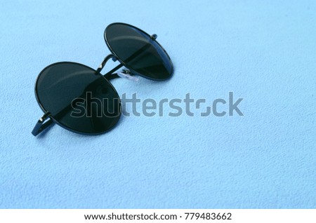 Stylish black sunglasses with round glasses lies on a blanket made of soft and fluffy light blue fleece fabric. Fashionable background picture in female colors