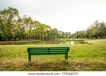 The bench on the grass is trees and sky backdrop.
