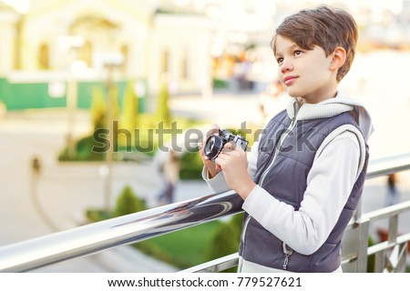 Cute young boy holding photocamera looking away thougthfully while travelling European city copyspace vacation journey happiness recreation positivity photography memories children kids childhood