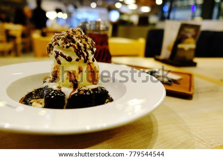 Chocolate mud brownie and vanilla ice cream with whipped cream on white plate at dessert shop. Delicious dessert with space for text. Concept be used for bakery and coffee shop business. Blur picture.