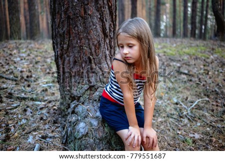 Little beautiful girl sitting on a stump in a pine forest in the summer time