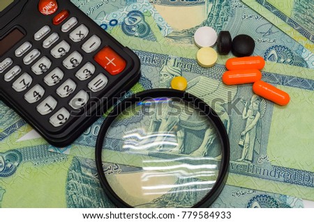magnifying glass, medication and calculator on uncirculated iraqi dinar (IQD) isolated on white