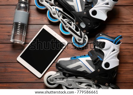 Roller skates, tablet computer and bottle of water on wooden background