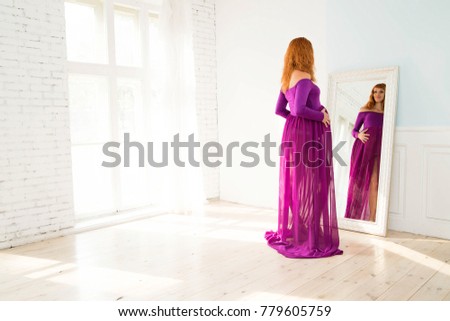 photo of pregnant woman in purple dress looks in mirror
