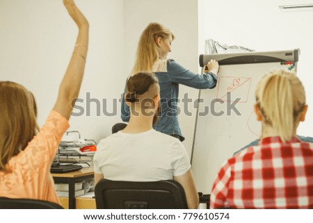 Group of students taking a part in maths lesson while sitting in lecture hall. Young teacher teaching mathematics, writing math formulas on the board