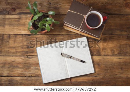 Picture of a diary and pens and a cap with tea on a pile of books on a wooden table
