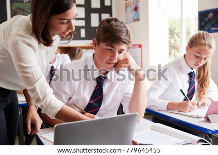 Female Teacher Helping Pupil Using Computer In Classroom Royalty-Free Stock Photo #779645455