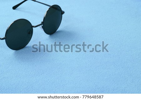Stylish black sunglasses with round glasses lies on a blanket made of soft and fluffy light blue fleece fabric. Fashionable background picture in female colors