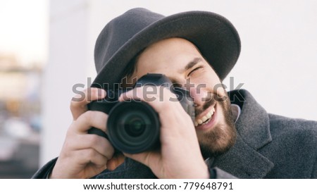 Closeup of happy paparazzi man in hat photographing celebrities on camera and smiling outdoors