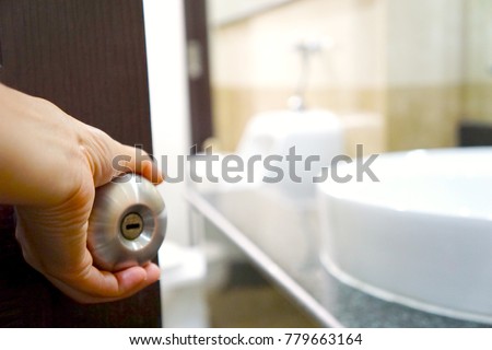 Close up left hand woman holding door handle to open the toilet. Can see sink and flush. Copy space. Royalty-Free Stock Photo #779663164