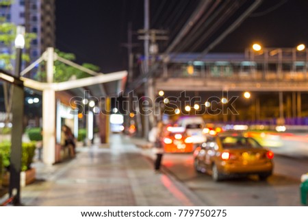 Blurry picture of an Asian woman waiting for a bus at bus stop by the street at night.