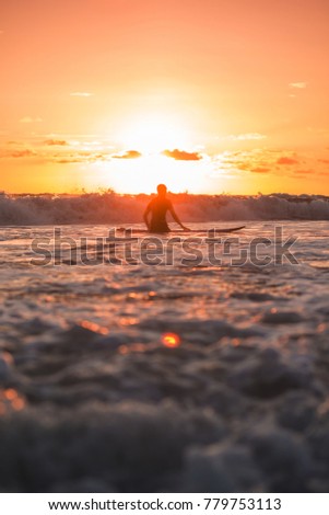 A surfer standing  in front of the sun