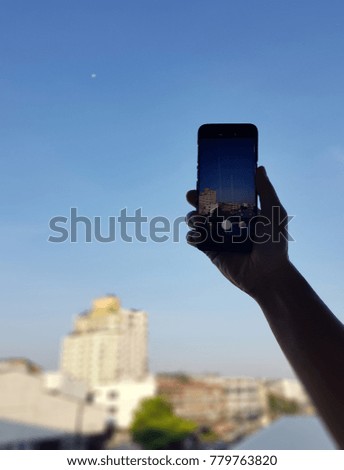 silhouette of hand's man taking a picture of a buildings and blue sky with his smart phone