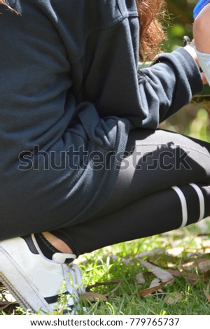 side perspective view of a young person in squat position over a fresh green grass wearing white sports shoes and dark black leggins and a navy blue sweater 