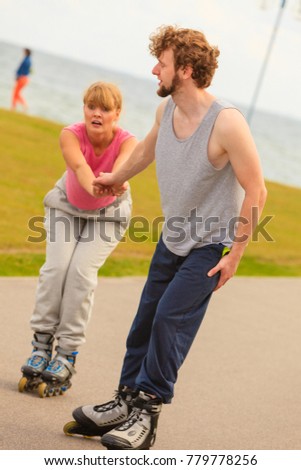 Roller skating couple during spare time in the park. Two people promote healthy lifestyle, enjoy good weather. Girl is terrified, boy takes care of her.