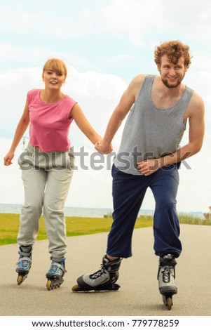 Active holidays, exercises, relationship concept. Young man dressed in sports clothes putting his girlfriend up to do rollerblading while holding her hand on promenade
