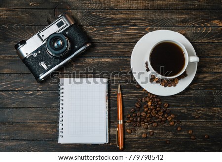 a cup of coffee in a saucer, coffee beans, isolated on a wooden background. business concept.
pen notebook.
camera